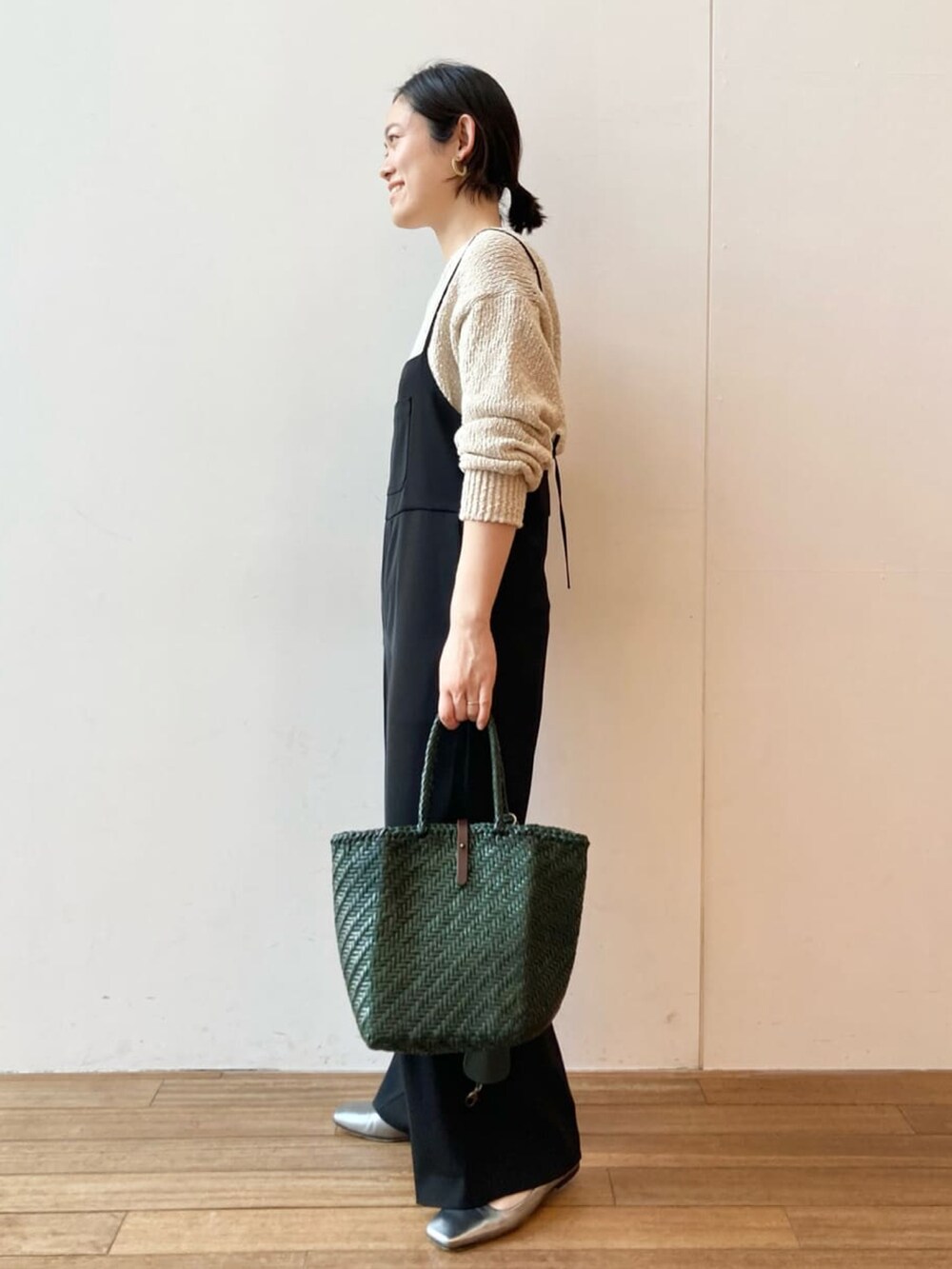 ベージュ系のニット/セーター、ブラック系のサロペット/オーバーオール、グリーン系のトートバッグを着用したレディースの春コーディネートの3枚目の写真