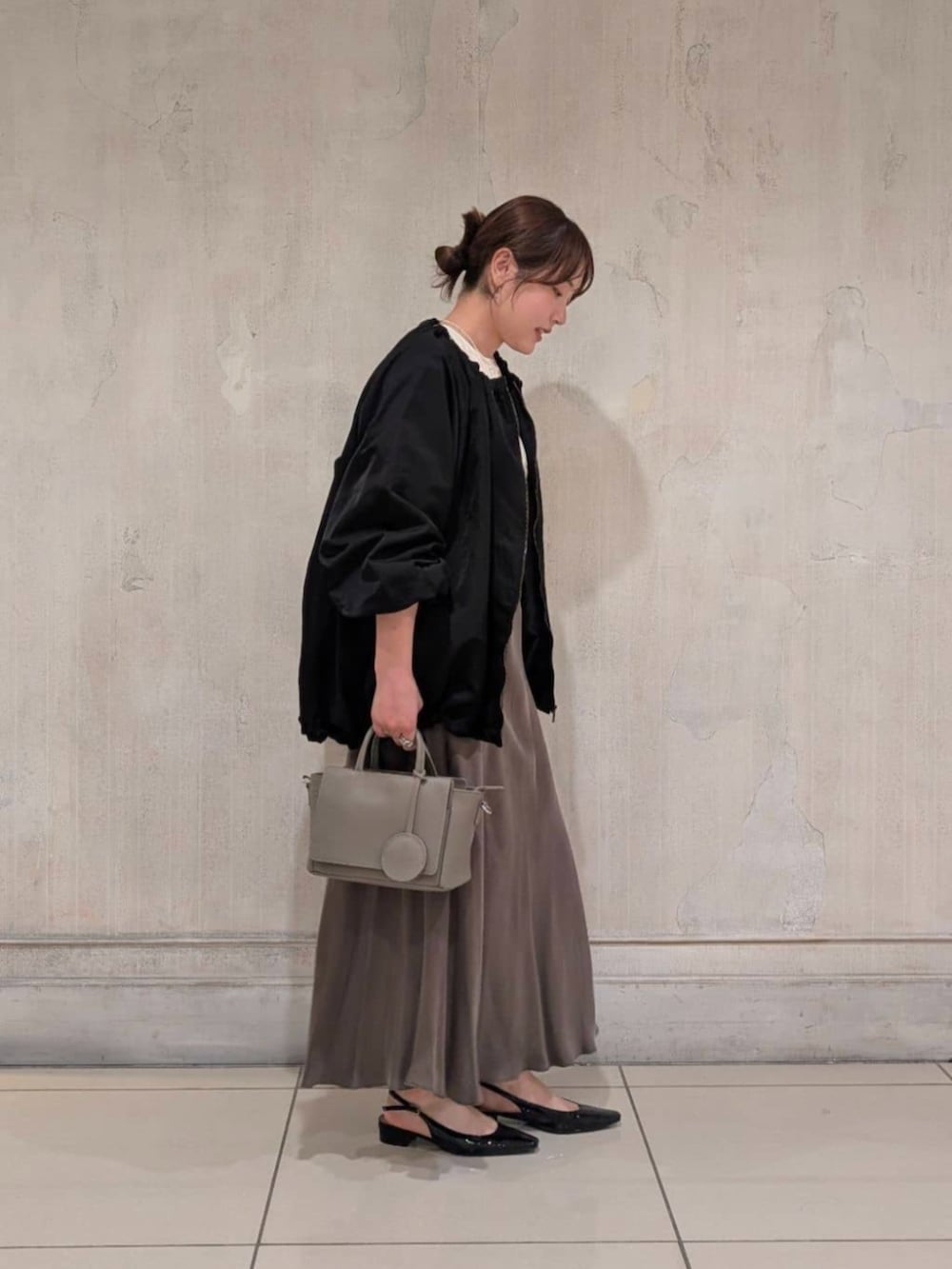 グリーン系のスカート、グレー系のハンドバッグ、ブラック系のノーカラージャケットを着用したレディースの春コーディネートの3枚目の写真