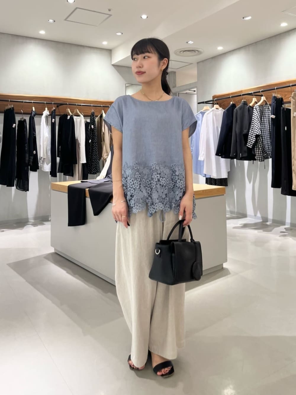 ブラック系のハンドバッグ、ベージュ系のその他パンツ、ブルー系のシャツ/ブラウスを着用したレディースの夏コーディネートの3枚目の写真
