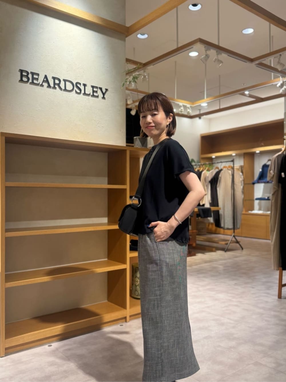 ブラック系のショルダーバッグ、ベージュ系のスカート、ゴールド系のネックレスを着用したレディースの春コーディネートの8枚目の写真