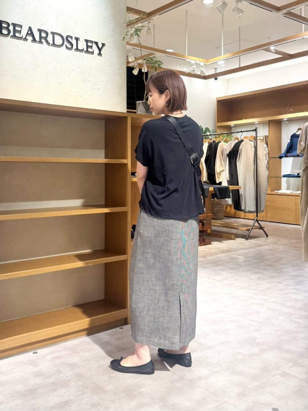 ブラック系のショルダーバッグ、ベージュ系のスカート、ゴールド系のネックレスを着用したレディースの春コーディネートの6枚目の写真