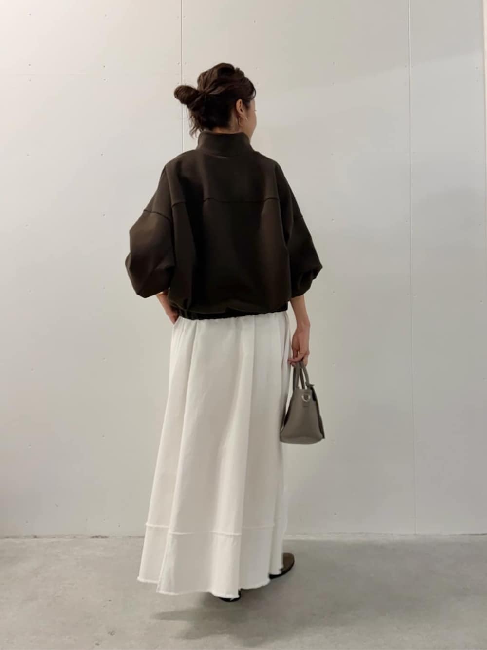 グレー系のハンドバッグ、ホワイト系のスカート、ブラウン系のTシャツ/カットソーを着用したレディースの夏コーディネートの3枚目の写真