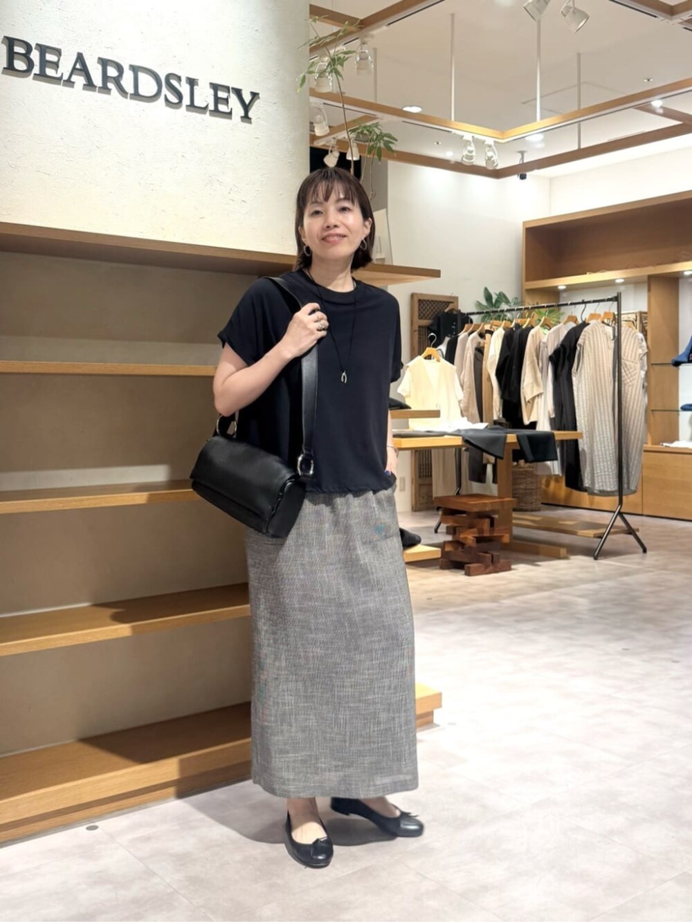 ブラック系のショルダーバッグ、ベージュ系のスカート、ゴールド系のネックレスを着用したレディースの春コーディネートの3枚目の写真