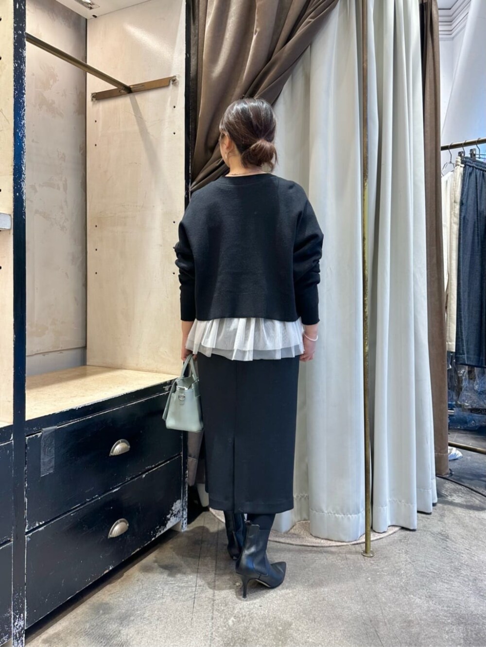 グリーン系のハンドバッグ、ブラック系のスカート、ブラック系のブーツを着用したレディースの冬コーディネートの4枚目の写真