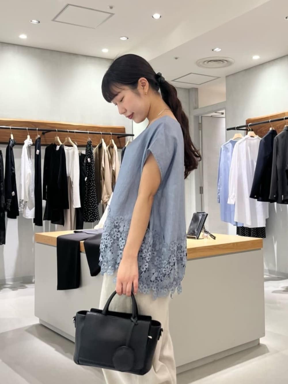 ブラック系のハンドバッグ、ベージュ系のその他パンツ、ブルー系のシャツ/ブラウスを着用したレディースの夏コーディネートの5枚目の写真
