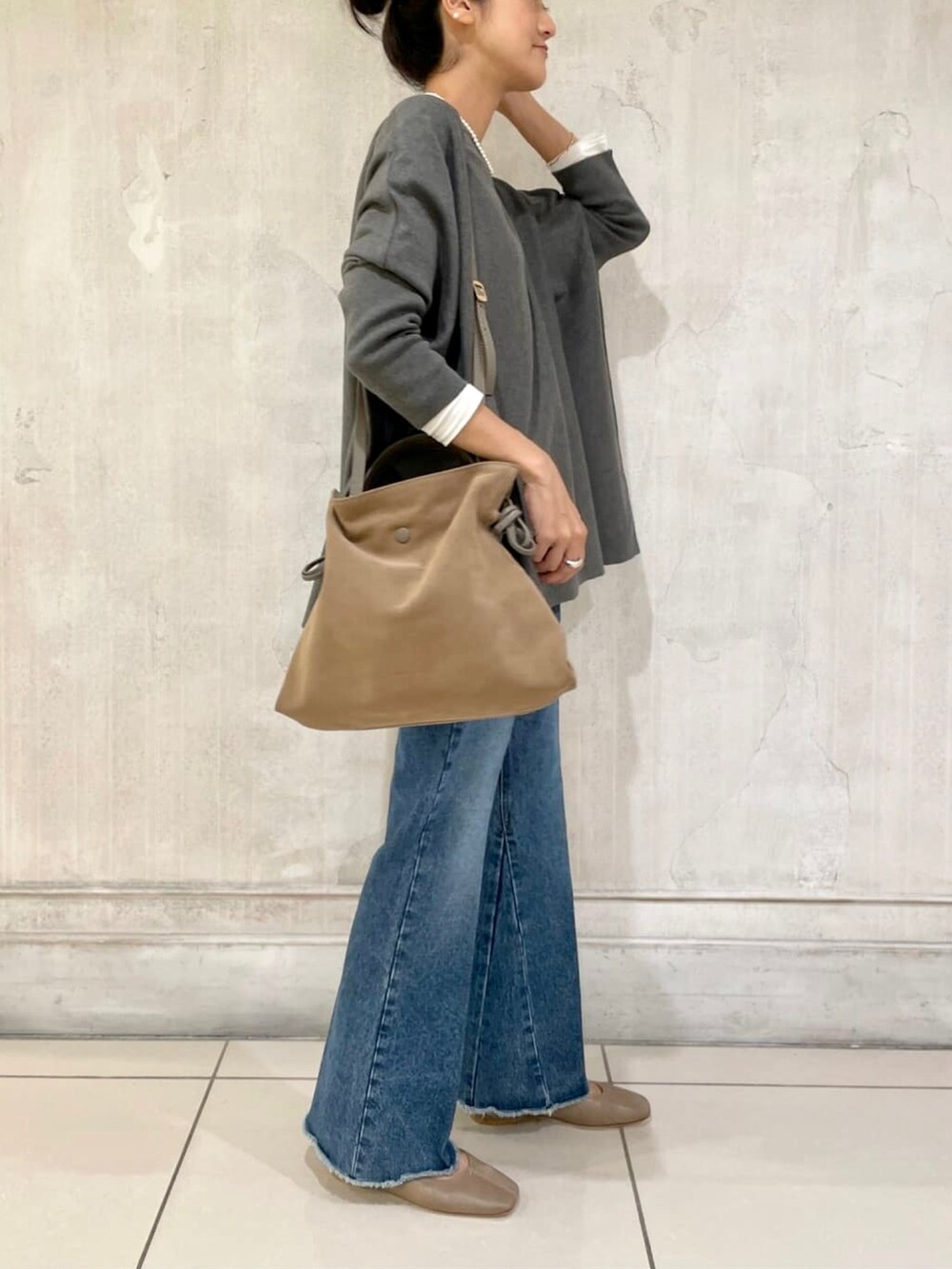 グレー系のニット/セーター、ブルー系のデニムパンツ、ブラウン系のショルダーバッグを着用したレディースの秋コーディネートの2枚目の写真