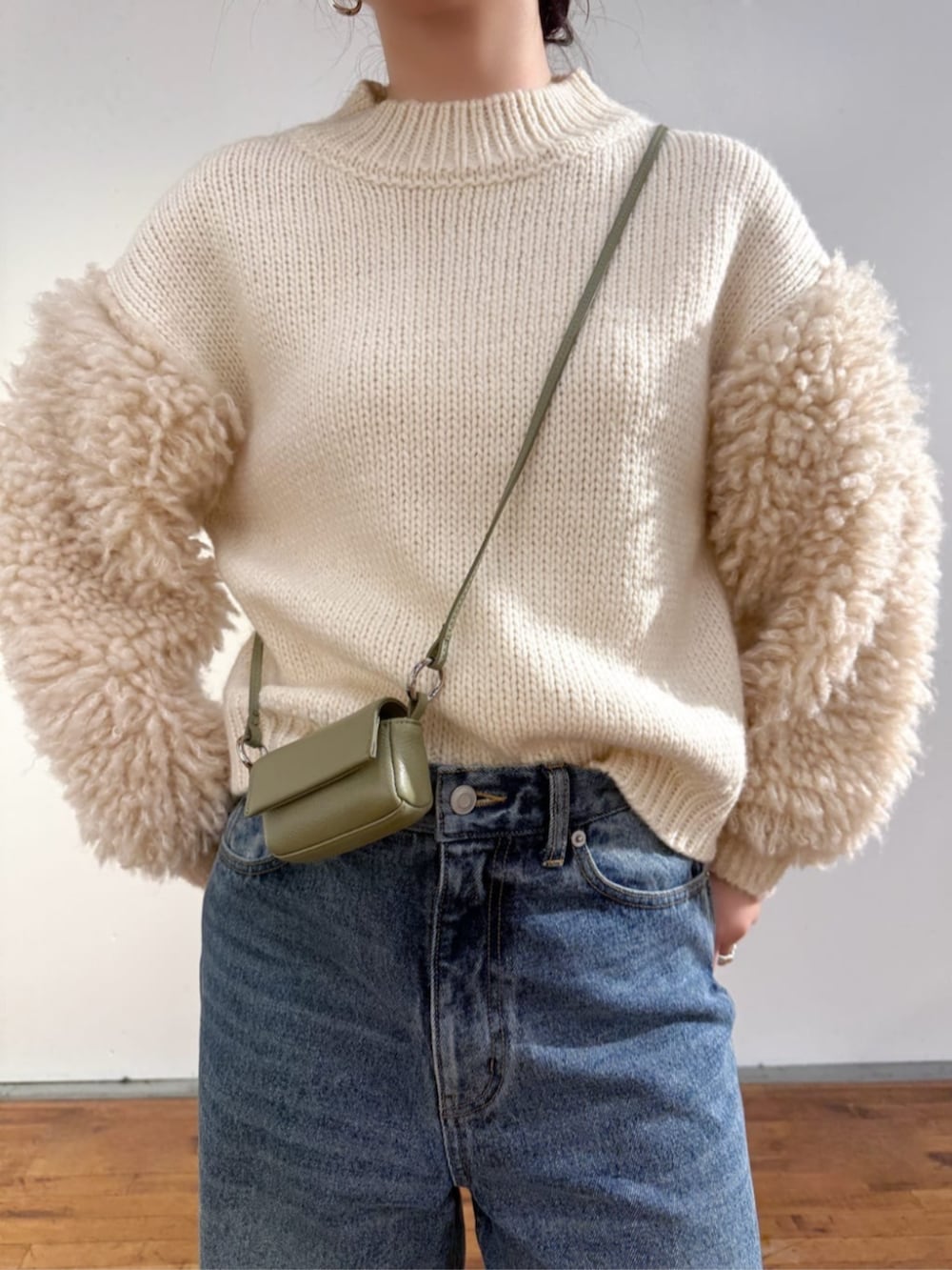 ブルー系のデニムパンツ、ホワイト系のニット/セーター、グリーン系のポーチを着用したレディースの秋コーディネートの2枚目の写真