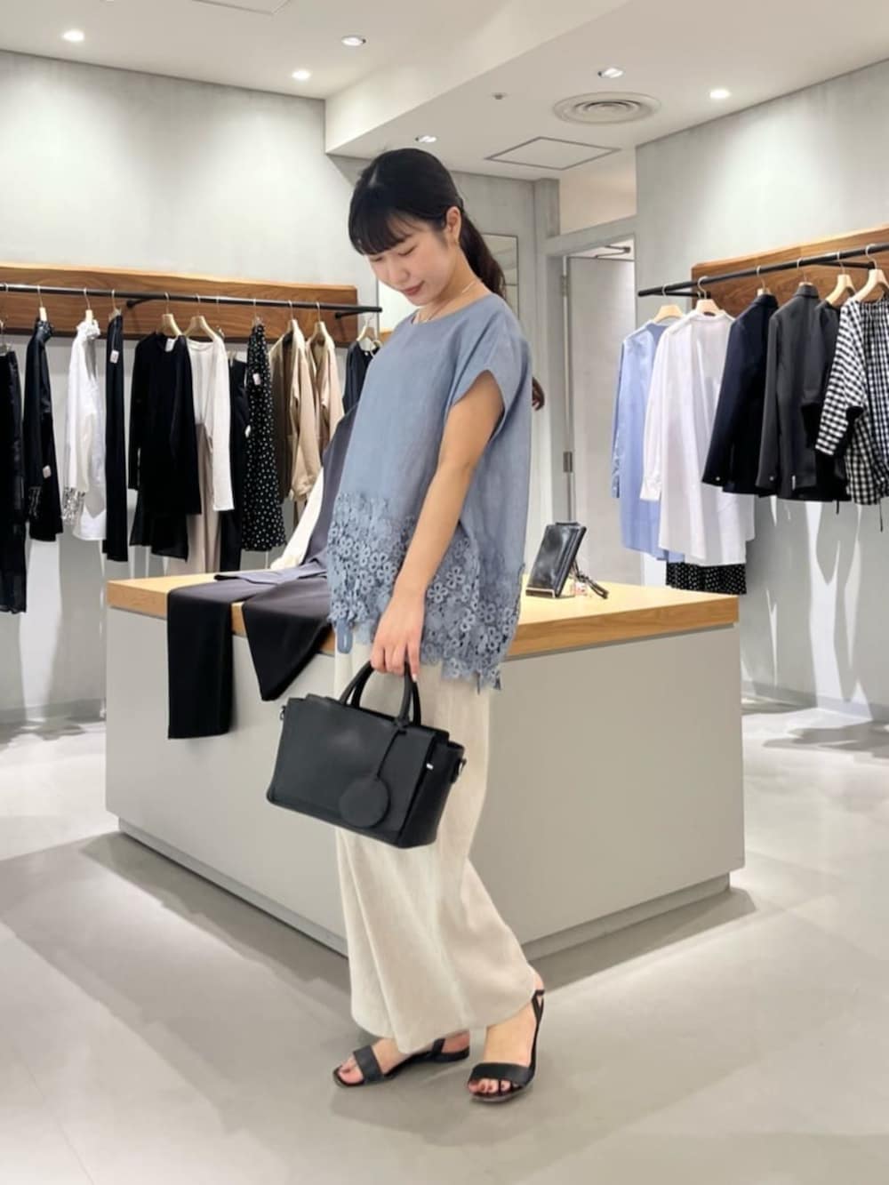 ブラック系のハンドバッグ、ベージュ系のその他パンツ、ブルー系のシャツ/ブラウスを着用したレディースの夏コーディネートの2枚目の写真
