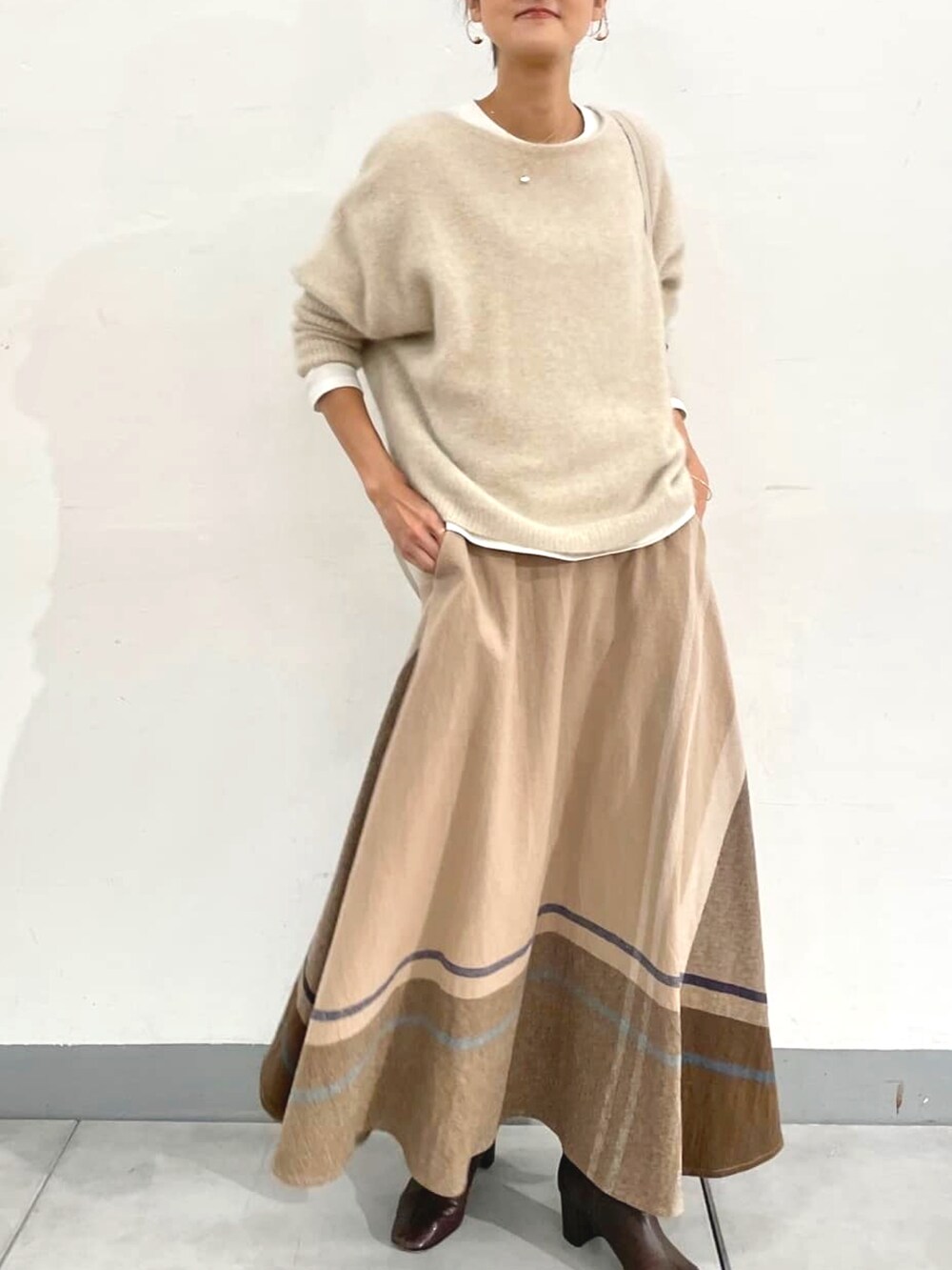 ホワイト系のニット/セーター、ホワイト系のTシャツ/カットソー、ベージュ系のスカートを着用したレディースの秋コーディネートの2枚目の写真