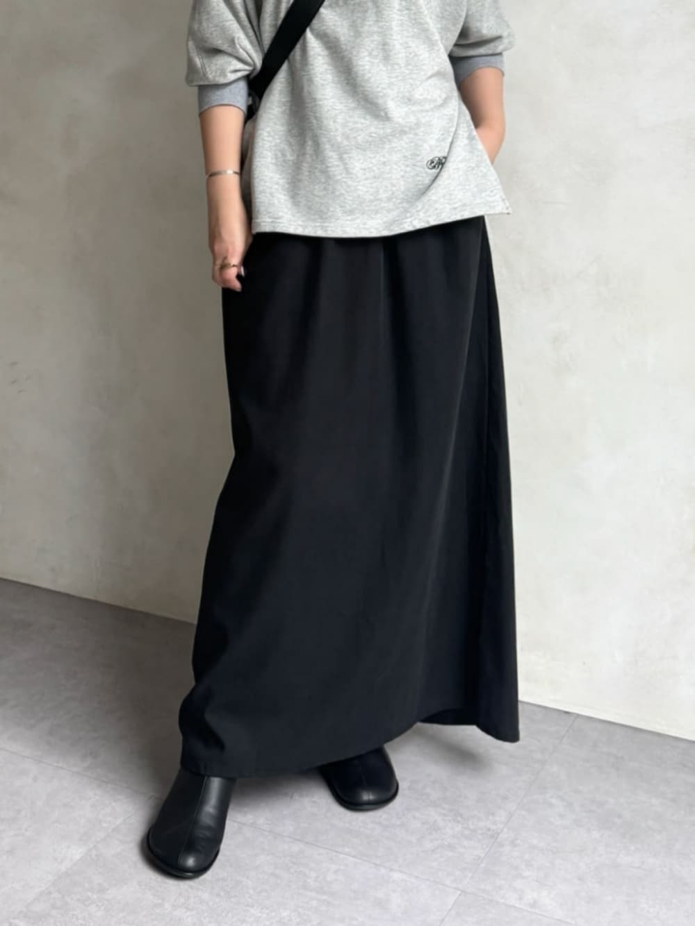 グレー系のTシャツ/カットソー、ブラック系のスカート、ブラック系のブーツを着用したレディースの秋コーディネートの5枚目の写真