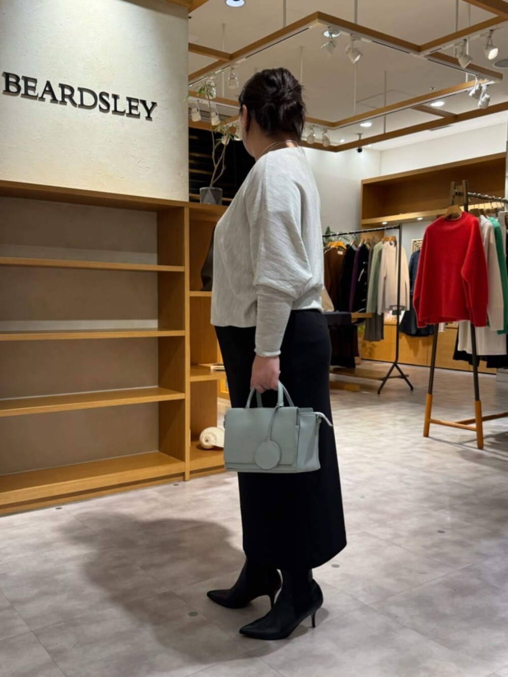 グリーン系のハンドバッグ、グレー系のニット/セーター、ブラック系のブーツを着用したレディースの冬コーディネートの2枚目の写真