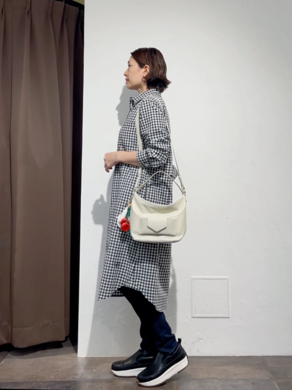 ブルー系のデニムパンツ、ブラック系のワンピース、ホワイト系のトートバッグを着用したレディースの春コーディネートの2枚目の写真