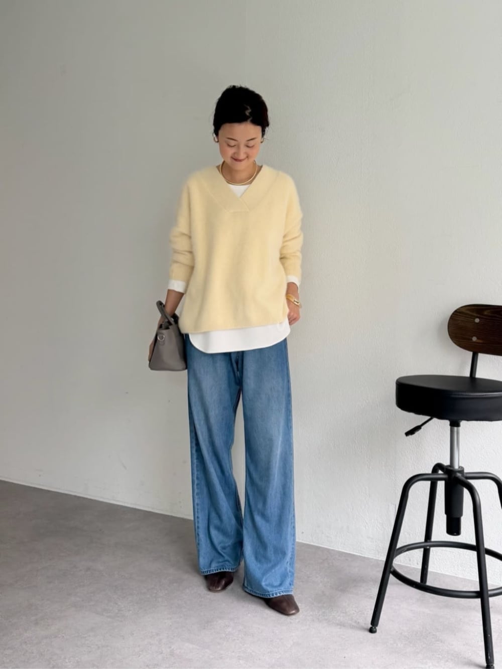 グレー系のハンドバッグ、ホワイト系のシャツ/ブラウス、イエロー系のニット/セーターを着用したレディースの秋コーディネートの2枚目の写真