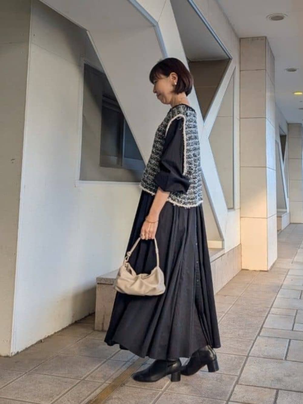 ベージュ系のショルダーバッグ、ブラック系のベスト、ブラック系のワンピースを着用したレディースの冬コーディネートの2枚目の写真