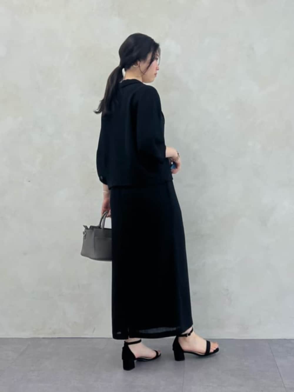 グレー系のハンドバッグ、ブラック系のテーラードジャケット、ブラック系のスカートを着用したレディースの春コーディネートの2枚目の写真
