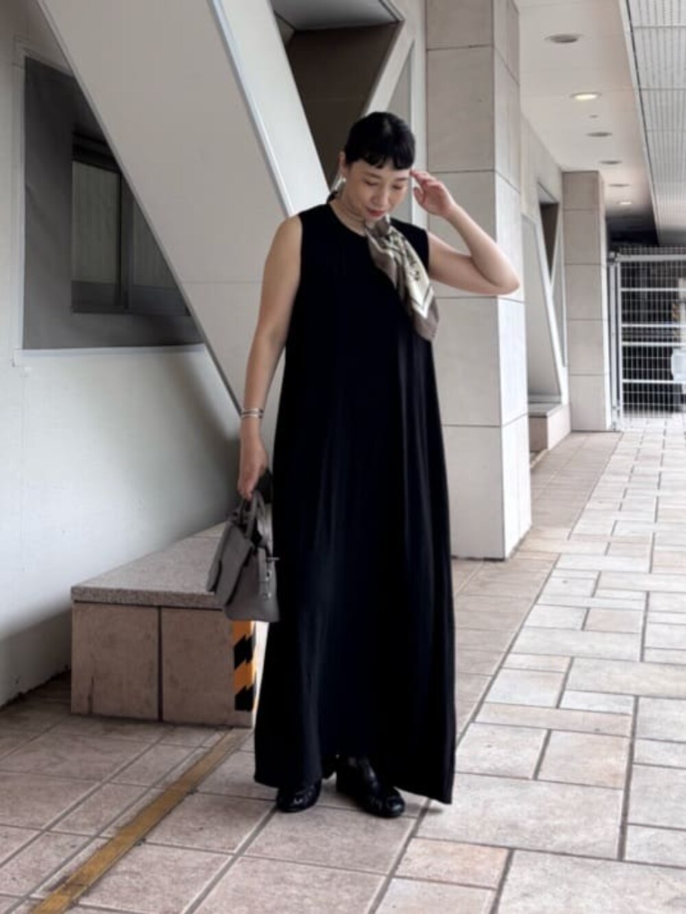 グレー系のハンドバッグ、ブラック系のサンダル、ブラック系のワンピースを着用したレディースの夏コーディネートの7枚目の写真