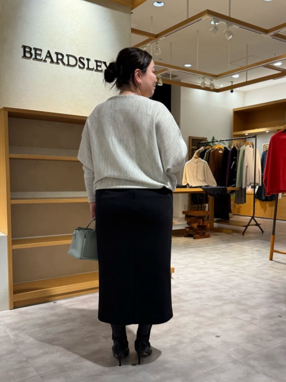 グリーン系のハンドバッグ、グレー系のニット/セーター、ブラック系のブーツを着用したレディースの冬コーディネートの3枚目の写真