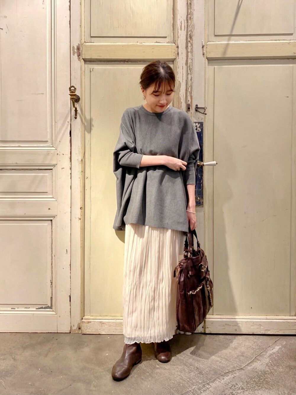 グレー系のニット/セーター、ホワイト系のスカート、ブラウン系のブーツを着用したレディースの秋コーディネートの4枚目の写真