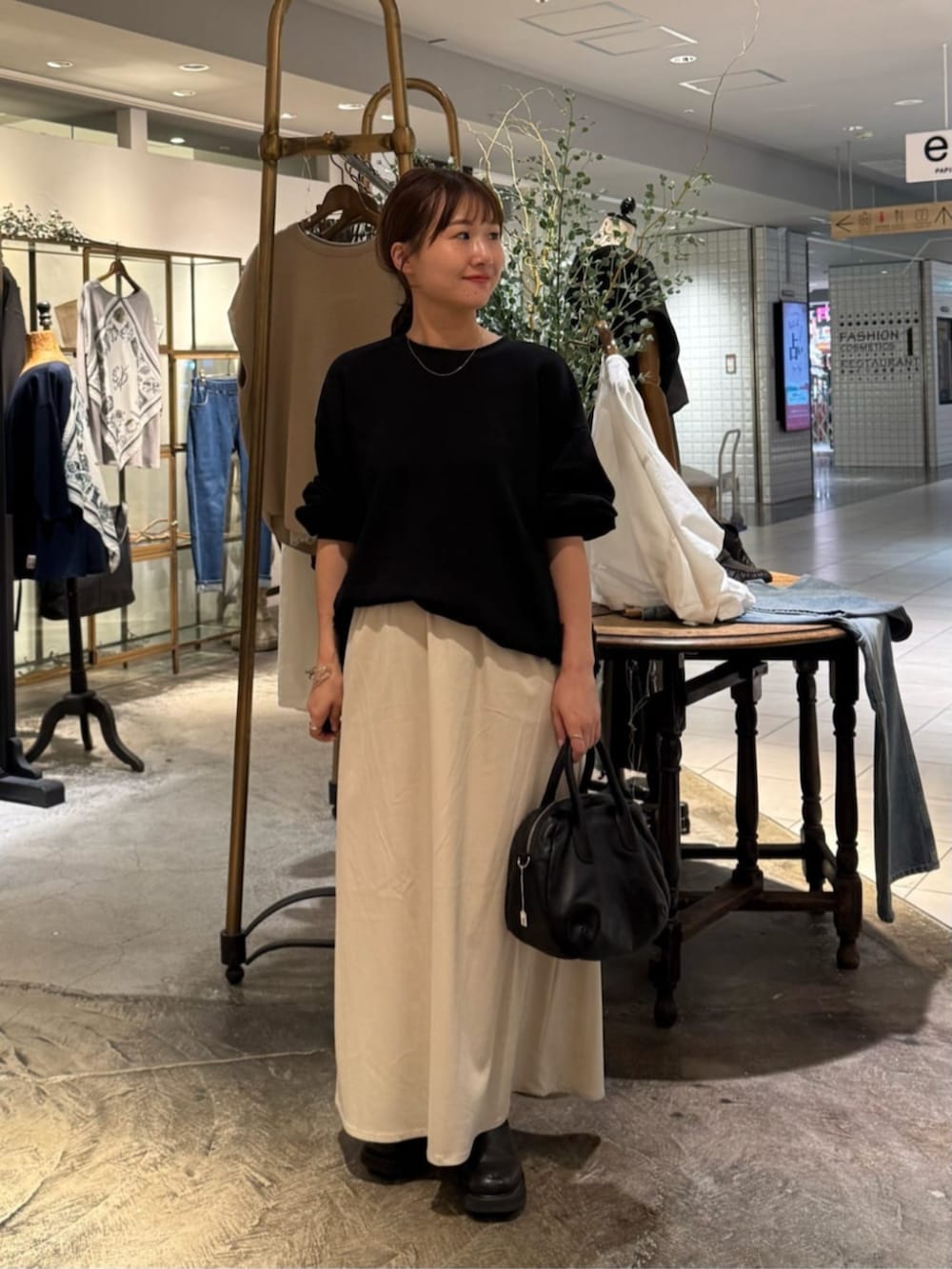 ブラック系のトートバッグ、ベージュ系のスカート、ブラック系のTシャツ/カットソーを着用したレディースの秋コーディネートの3枚目の写真