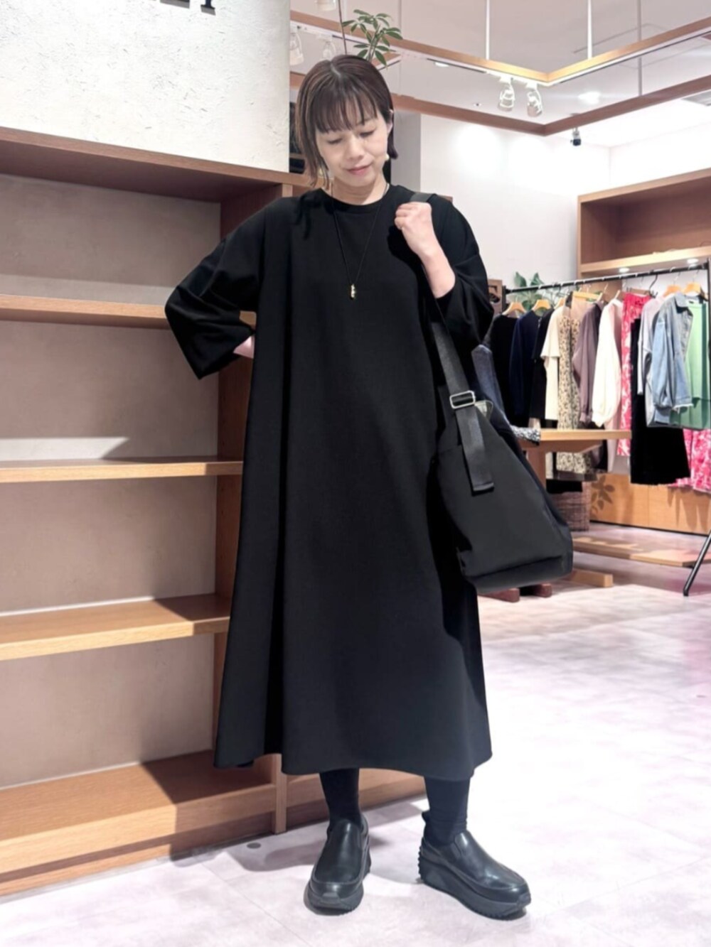 ブラック系のワンピース、ブラック系のトートバッグ、ホワイト系のポーチを着用したレディースの秋コーディネートの2枚目の写真