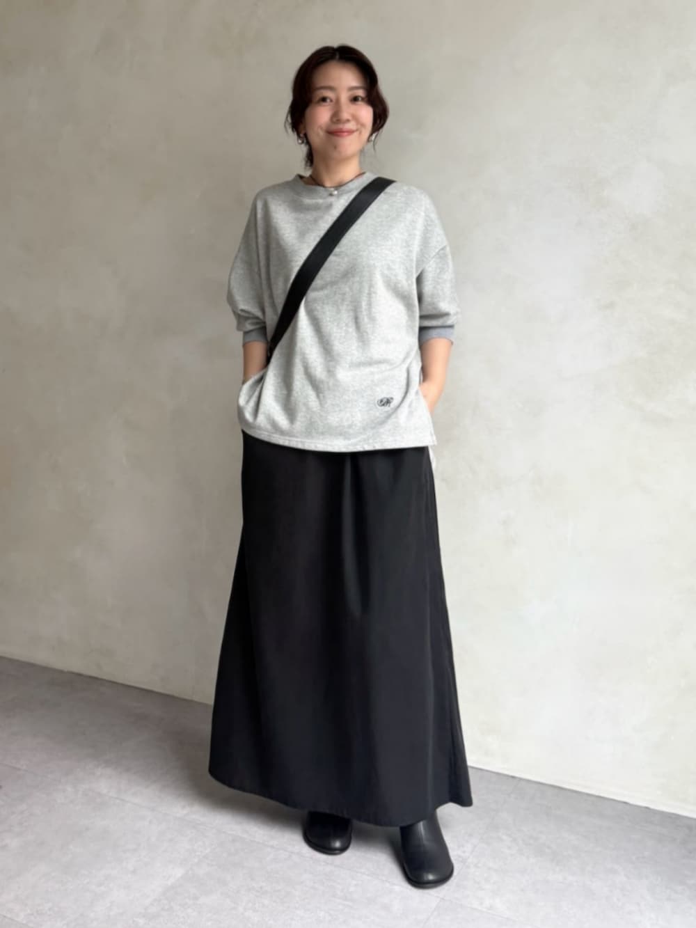 グレー系のTシャツ/カットソー、ブラック系のスカート、ブラック系のブーツを着用したレディースの秋コーディネートの2枚目の写真
