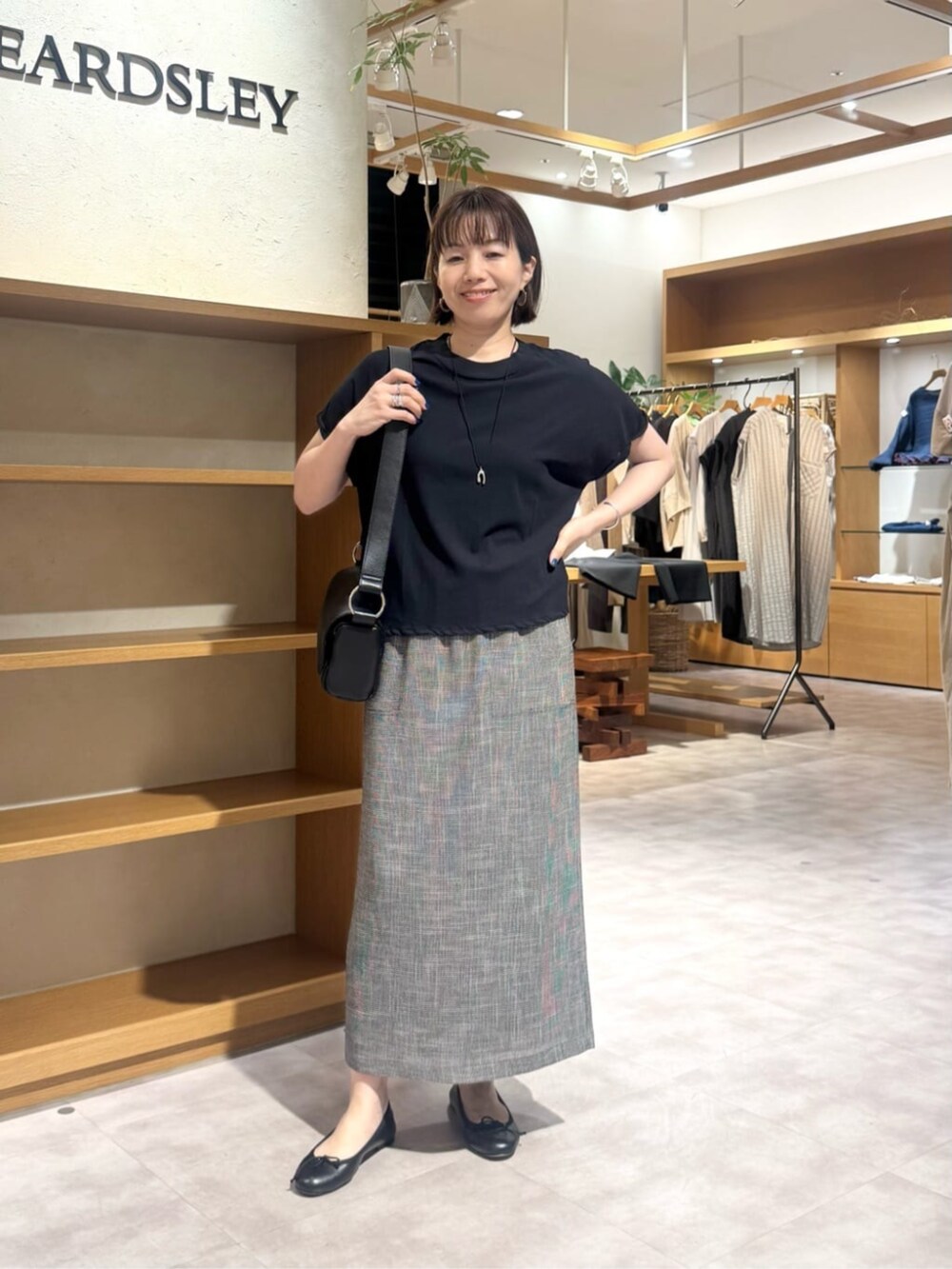 ブラック系のショルダーバッグ、ベージュ系のスカート、ゴールド系のネックレスを着用したレディースの春コーディネートの2枚目の写真