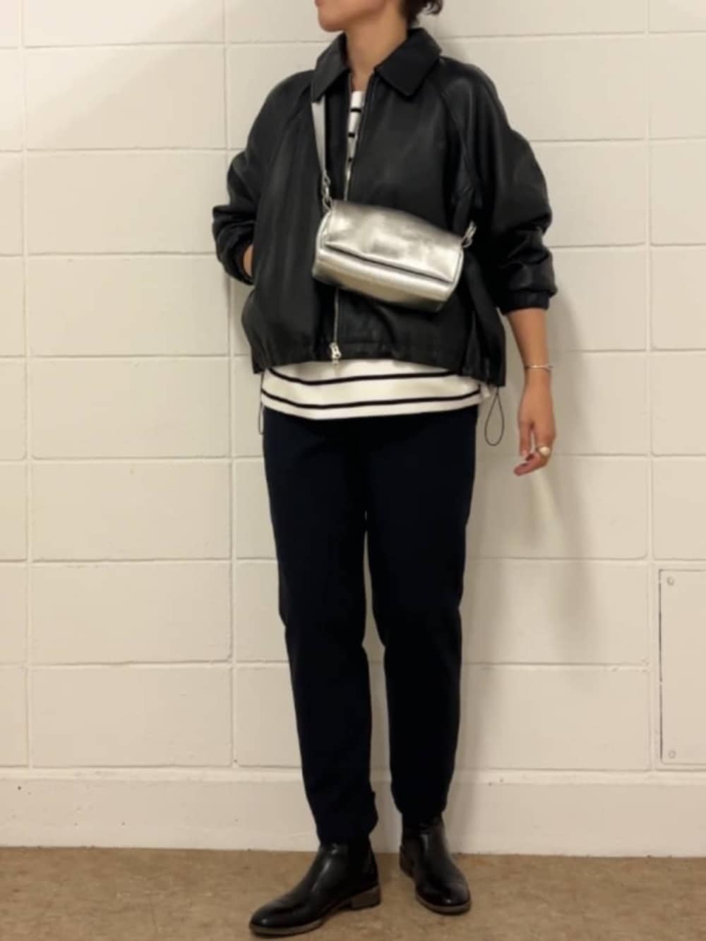 シルバー系のショルダーバッグ、ホワイト系のニット/セーター、ブラック系のブルゾンを着用したレディースの冬コーディネートの2枚目の写真