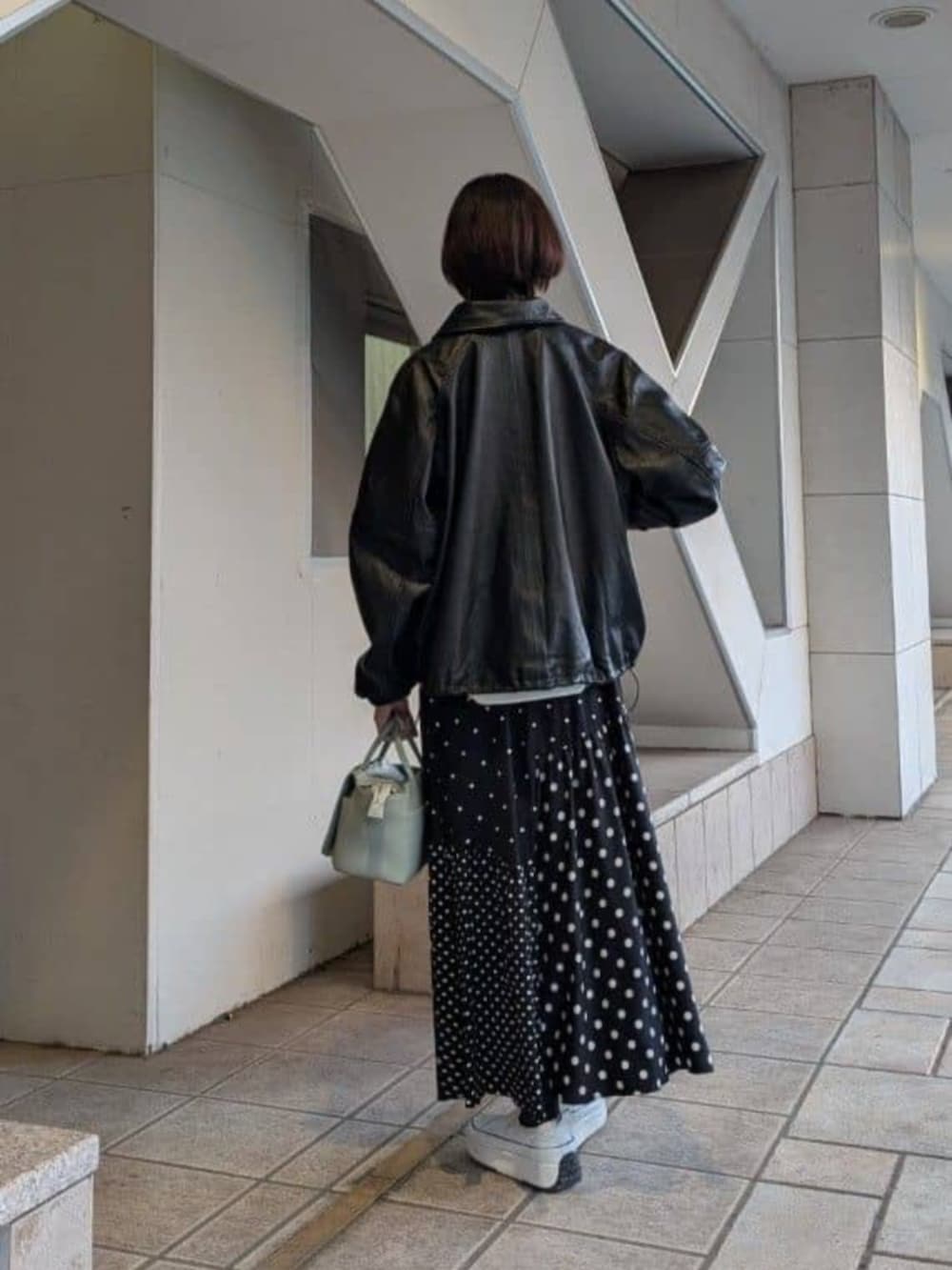 グリーン系のハンドバッグ、ブラック系のスカート、ブラック系のブルゾンを着用したレディースの冬コーディネートの3枚目の写真