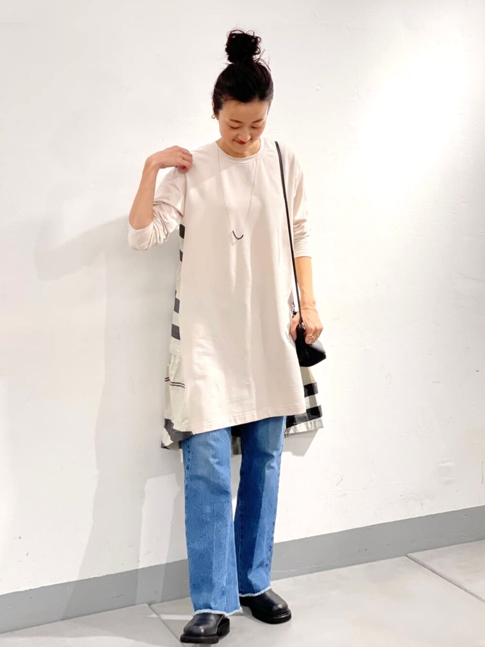 ホワイト系のワンピース、ホワイト系のショルダーバッグ、ブルー系のデニムパンツを着用したレディースの秋コーディネートの4枚目の写真