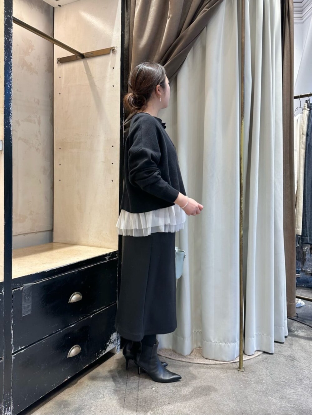 グリーン系のハンドバッグ、ブラック系のスカート、ブラック系のブーツを着用したレディースの冬コーディネートの2枚目の写真