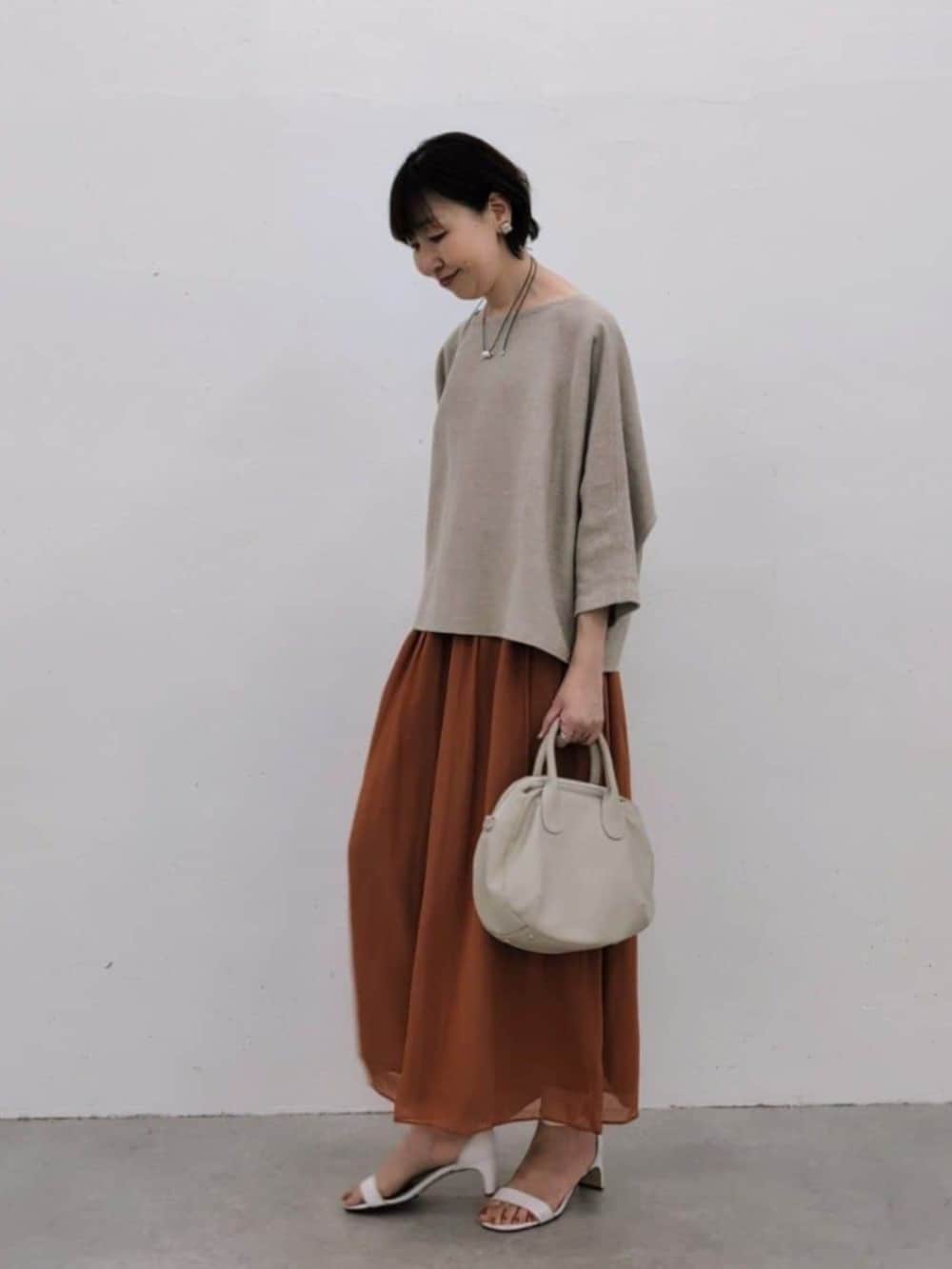 グレー系のボストンバッグ、オレンジ系のその他パンツ、ベージュ系のニット/セーターを着用したレディースの冬コーディネートの2枚目の写真