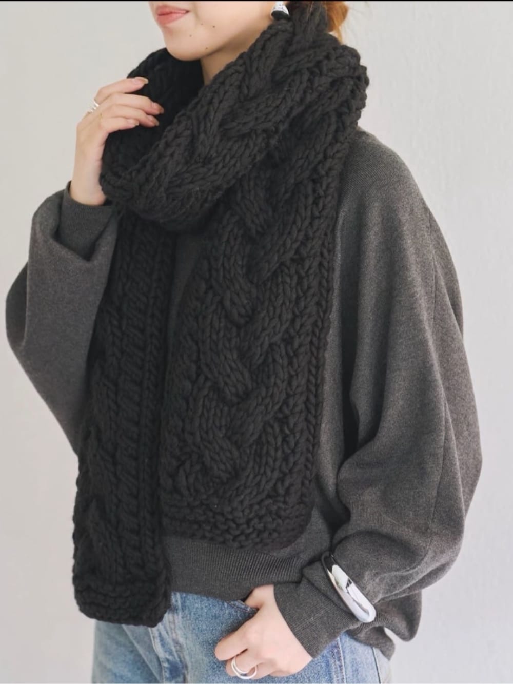 グレー系のニット/セーター、ブルー系のデニムパンツ、ブラック系のマフラーを着用したレディースの秋コーディネートの2枚目の写真