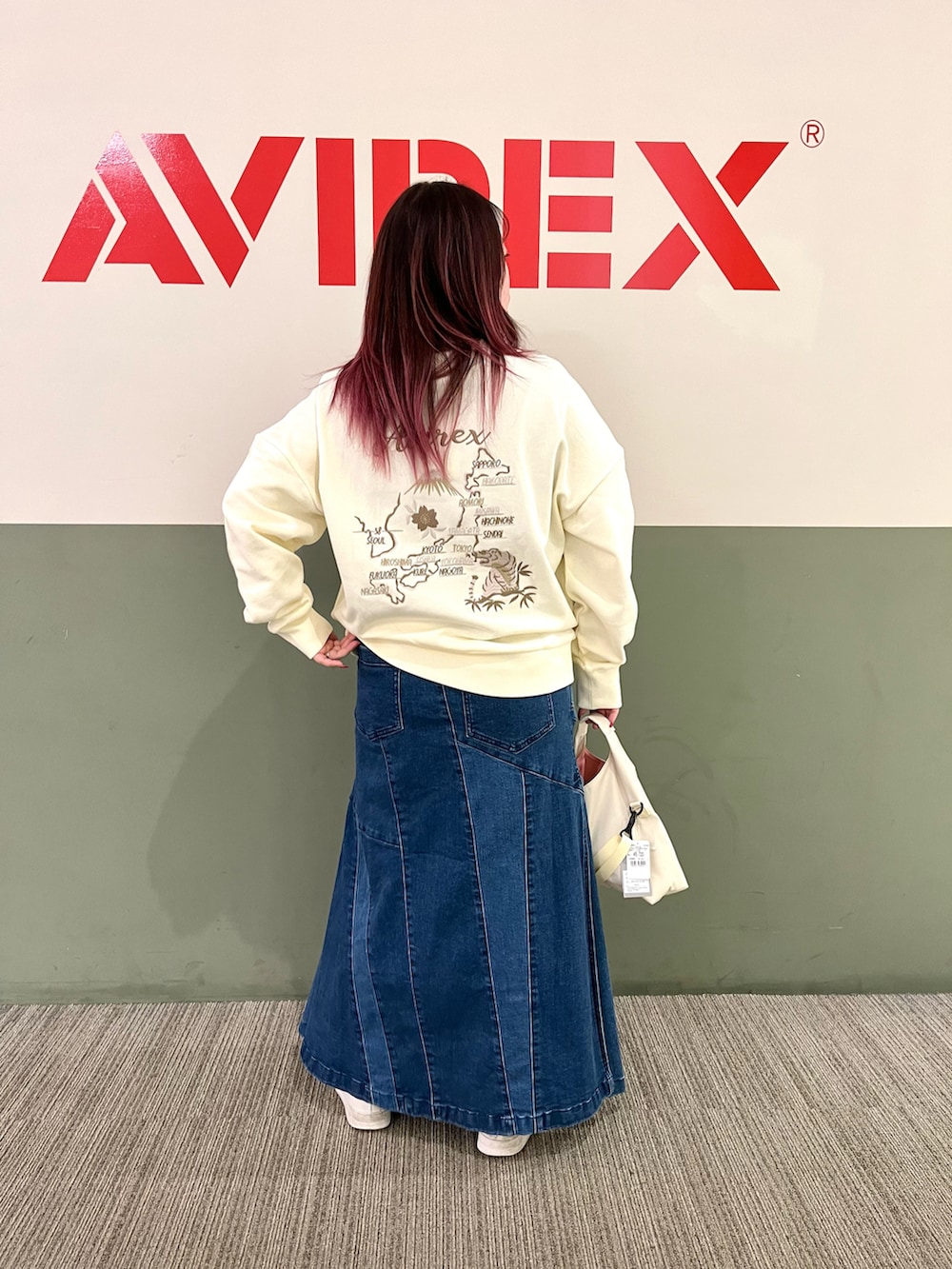 ホワイト系のスウェット、ブルー系のデニムスカート、グリーン系のショルダーバッグを着用したレディースの秋コーディネートの2枚目の写真