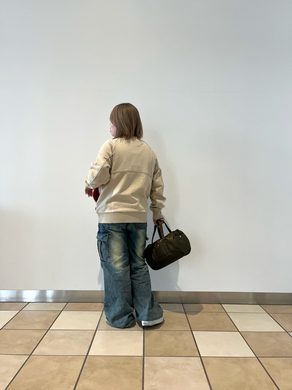 ベージュ系のスウェット、グリーン系のボストンバッグ、ブルー系のデニムパンツを着用したレディースの秋コーディネートの2枚目の写真