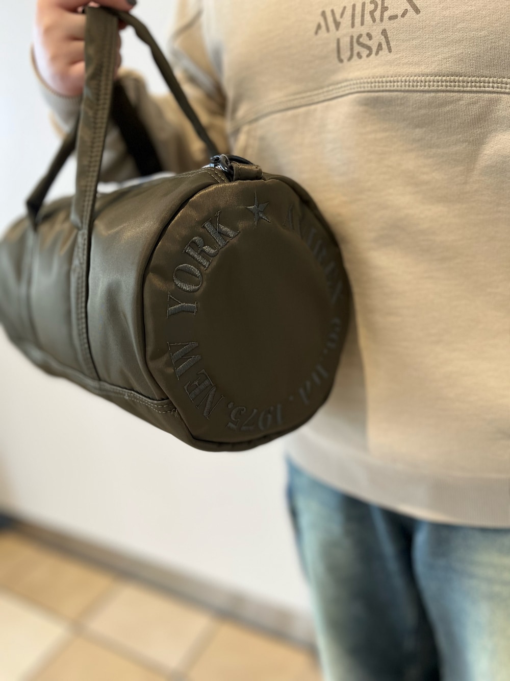 ベージュ系のスウェット、グリーン系のボストンバッグ、ブルー系のデニムパンツを着用したレディースの秋コーディネートの5枚目の写真