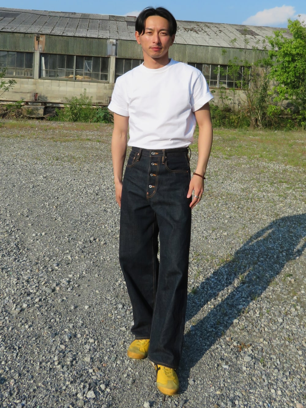 ブルー系のデニムパンツ、イエロー系のスニーカー、ホワイト系のTシャツ/カットソーを着用したメンズの春コーディネートの2枚目の写真