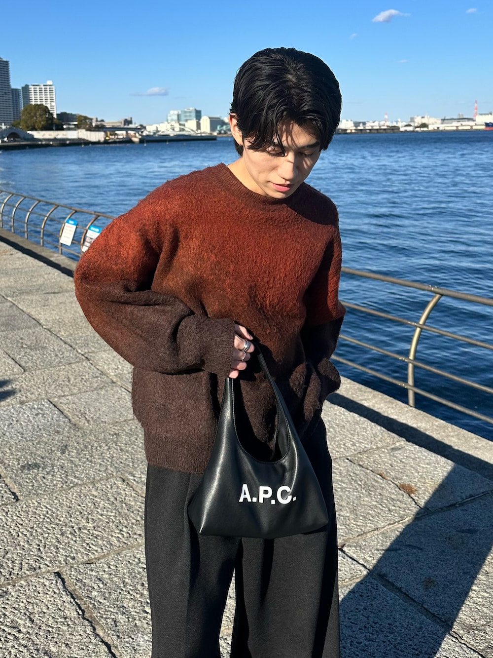 ブラウン系のニット/セーター、グレー系のスラックス、ブラック系のショルダーバッグを着用したメンズの冬コーディネートの2枚目の写真