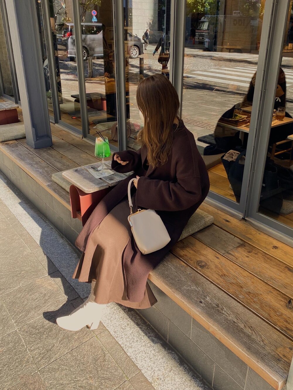 ブラウン系のノーカラーコート、ブラウン系のカーディガン/ボレロ、ベージュ系のショルダーバッグを着用したレディースの冬コーディネートの2枚目の写真