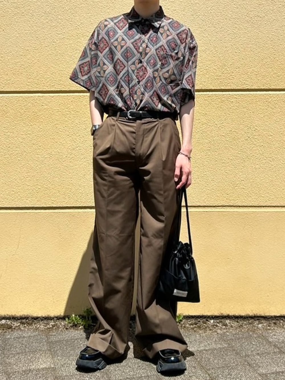 ブラック系のハンドバッグ、ブラウン系のスラックス、ブラック系のローファーを着用したメンズの春コーディネートの2枚目の写真