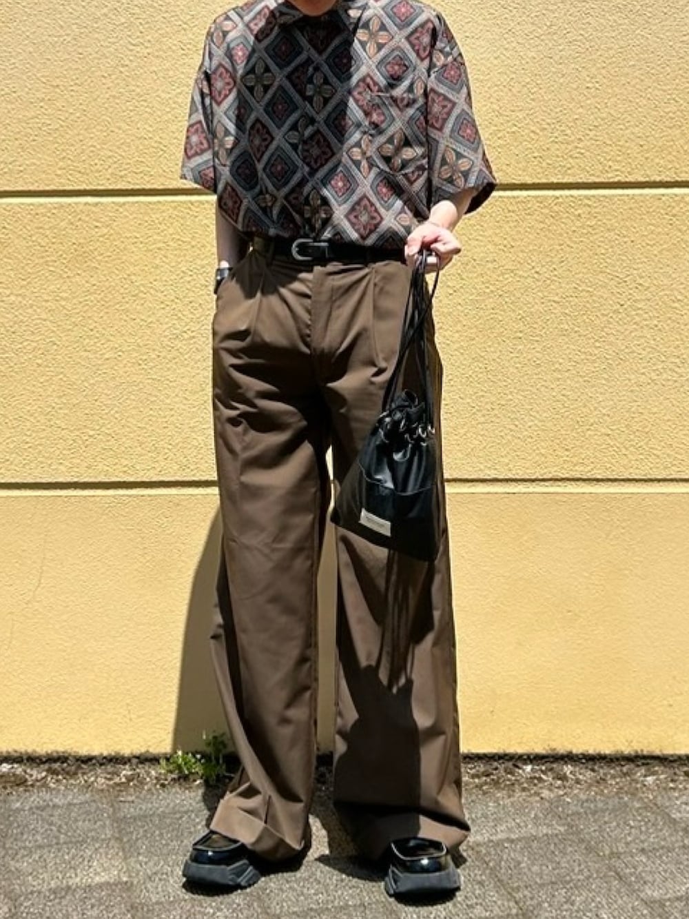 ブラック系のハンドバッグ、ブラウン系のスラックス、ブラック系のローファーを着用したメンズの春コーディネートの3枚目の写真