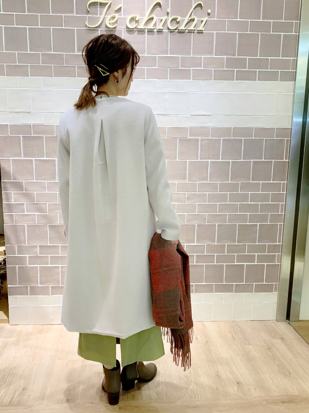 グリーン系のスカート、ベージュ系のノーカラーコート、ベージュ系のブーツを着用したレディースの冬コーディネートの2枚目の写真