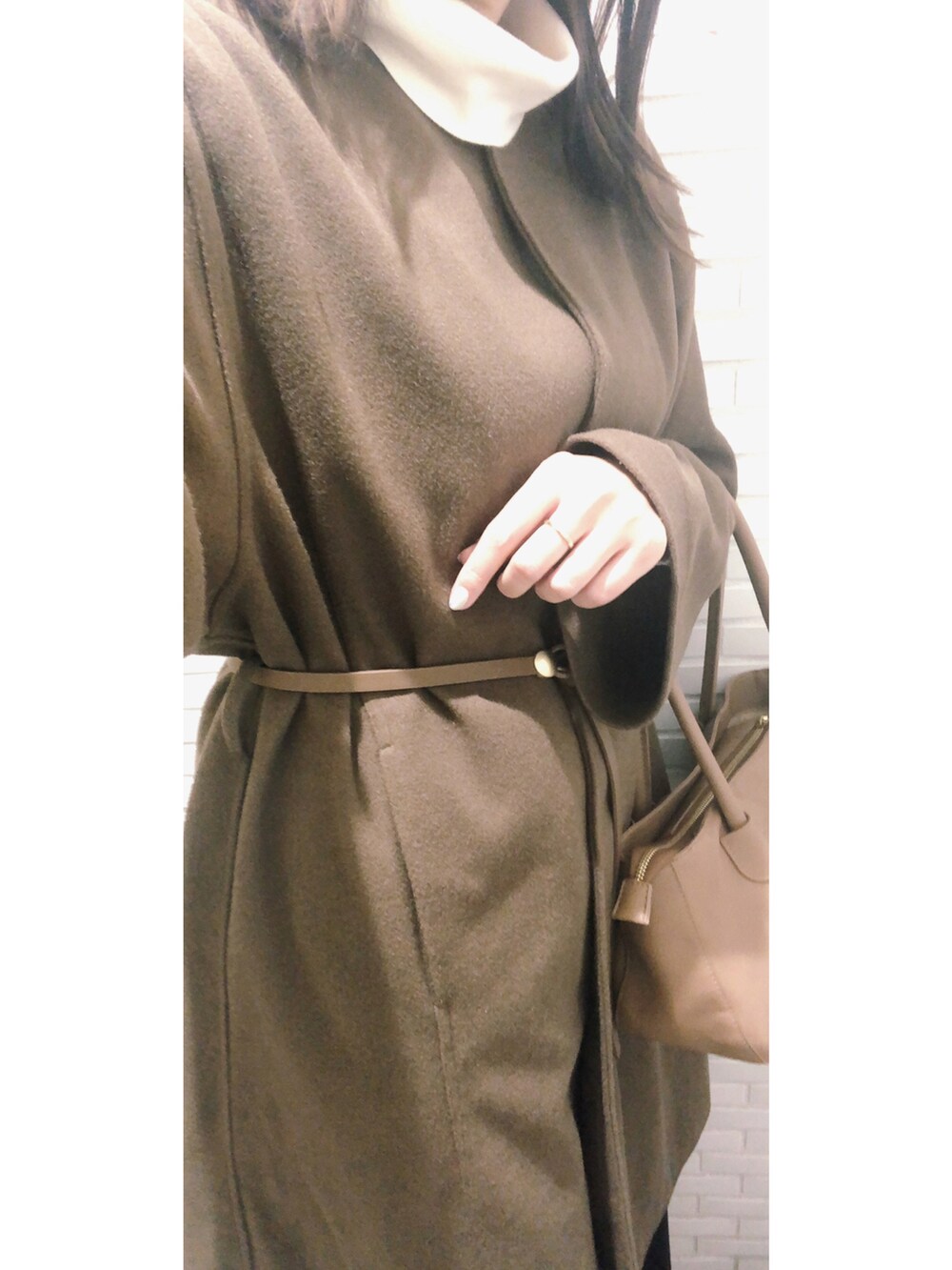 ブラウン系のノーカラーコート、ホワイト系のニット/セーター、ブラウン系のベルトを着用したレディースの冬コーディネートの2枚目の写真