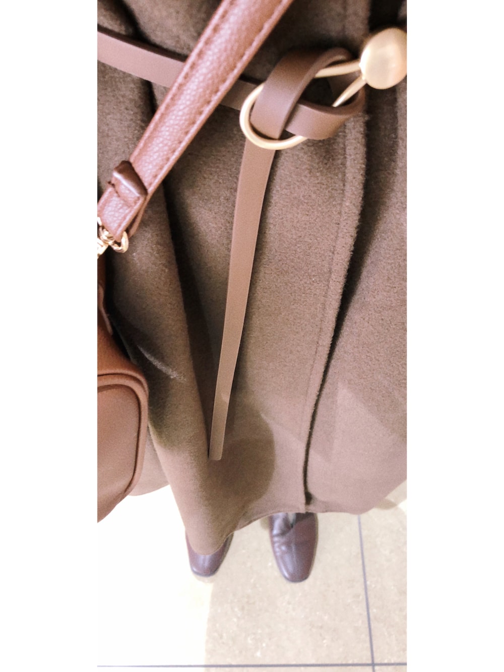 ブラウン系のノーカラーコート、ブラウン系のバッグ、ホワイト系のニット/セーターを着用したレディースの冬コーディネートの3枚目の写真