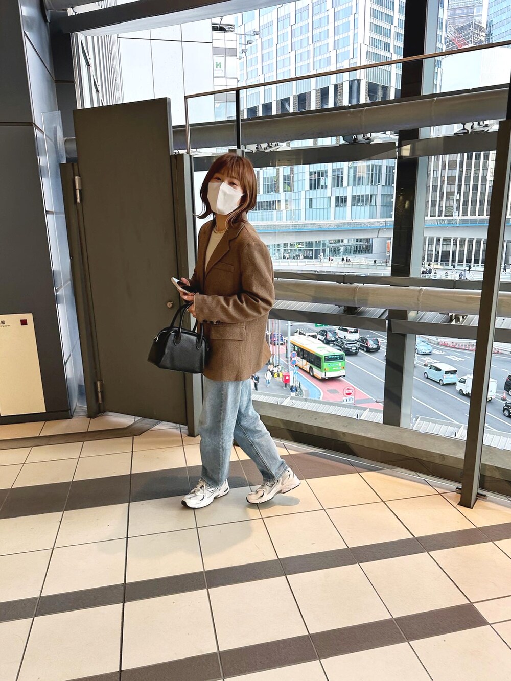 ブラウン系のテーラードジャケット、ブラック系のボストンバッグ、ブルー系のデニムパンツを着用したレディースの春コーディネートの2枚目の写真