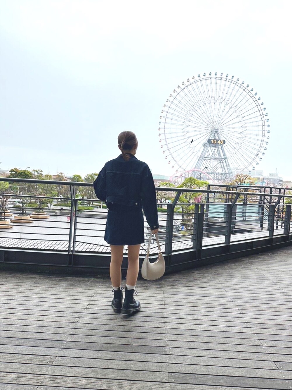 ブルー系のデニムジャケット、ホワイト系のハンドバッグ、ブラック系のブーツを着用したレディースの春コーディネートの3枚目の写真