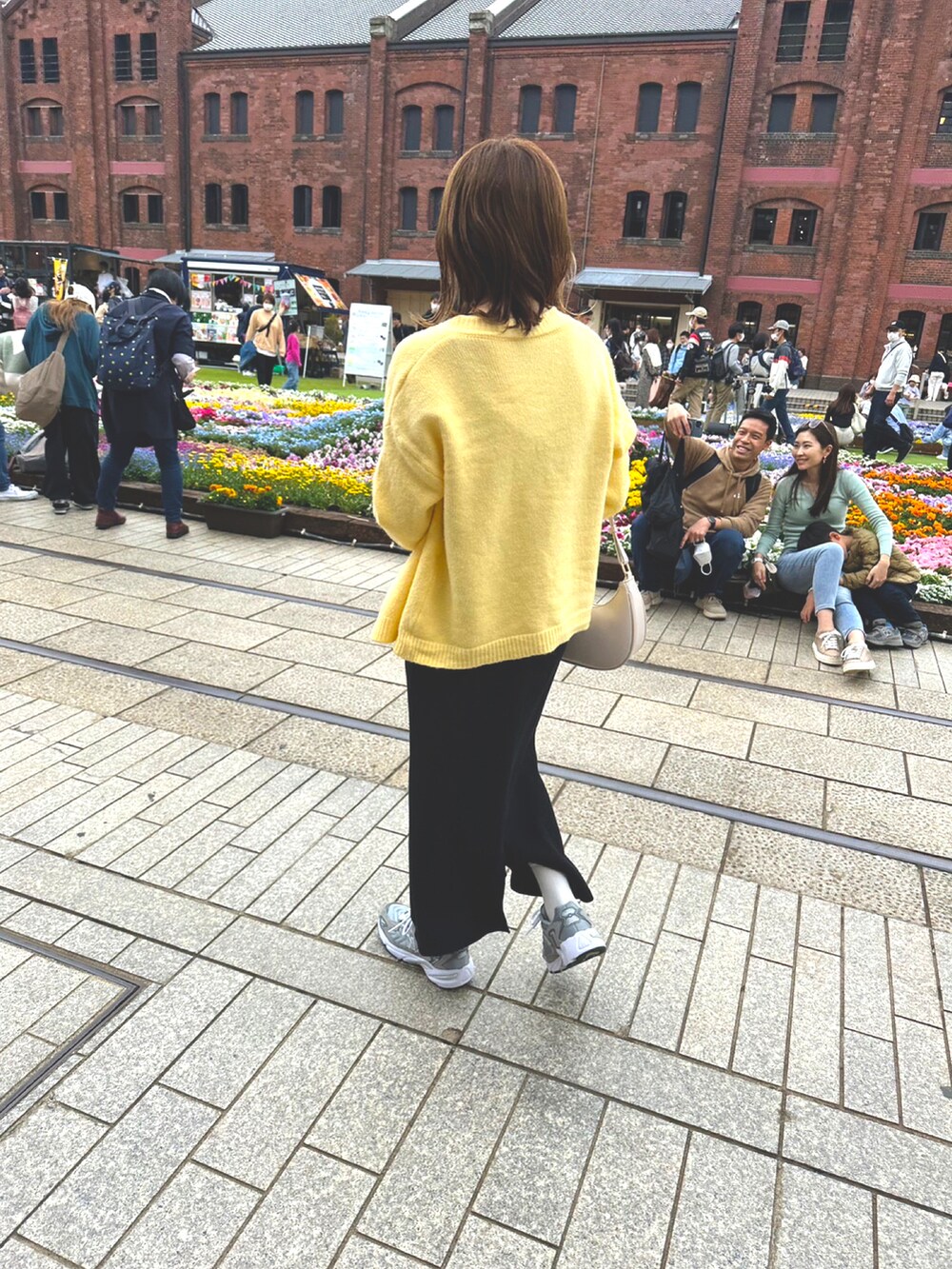 イエロー系のカーディガン/ボレロ、ブラック系のワンピース、グレー系のスニーカーを着用したレディースの春コーディネートの2枚目の写真