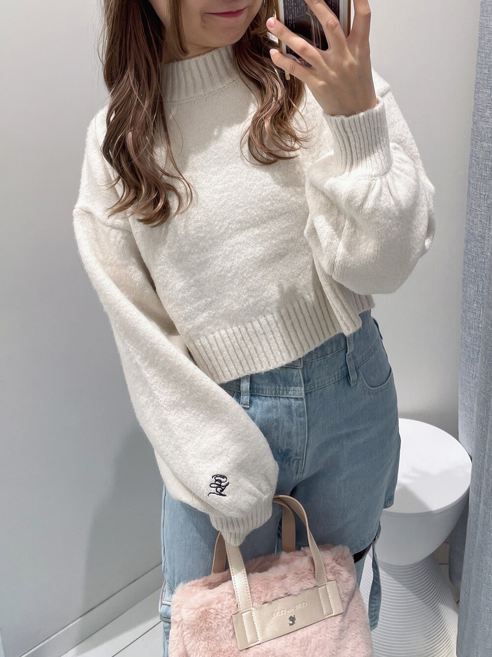 ピンク系のショルダーバッグ、ホワイト系のニット/セーター、ブルー系のデニムパンツを着用したレディースの秋コーディネートの2枚目の写真