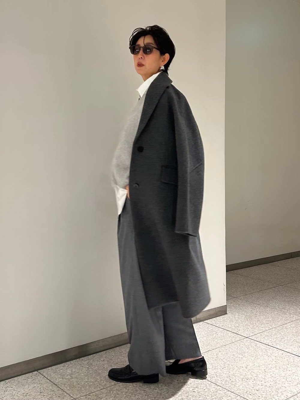 グレー系のニット/セーター、ホワイト系のシャツ/ブラウス、グレー系のスラックスを着用したレディースの秋コーディネートの3枚目の写真