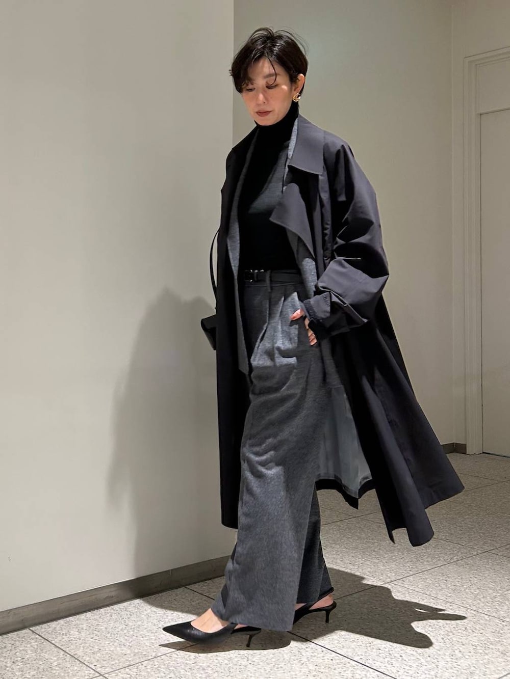 ブラック系のニット/セーター、ブラック系のトレンチコート、グレー系のスラックスを着用したレディースの秋コーディネートの2枚目の写真