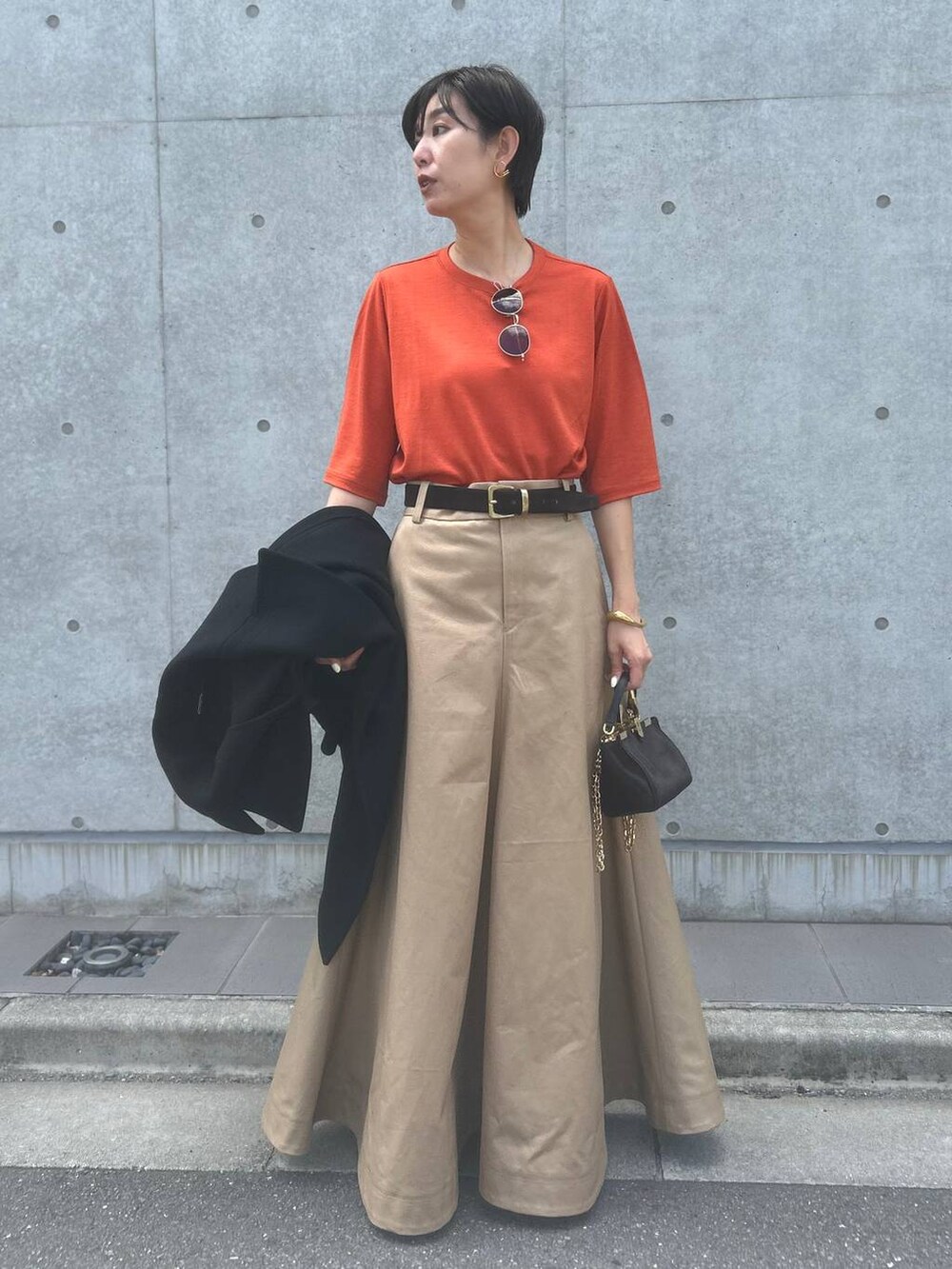 オレンジ系のTシャツ/カットソー、ベージュ系のスカート、ブラック系のその他アウターを着用したレディースの秋コーディネートの2枚目の写真